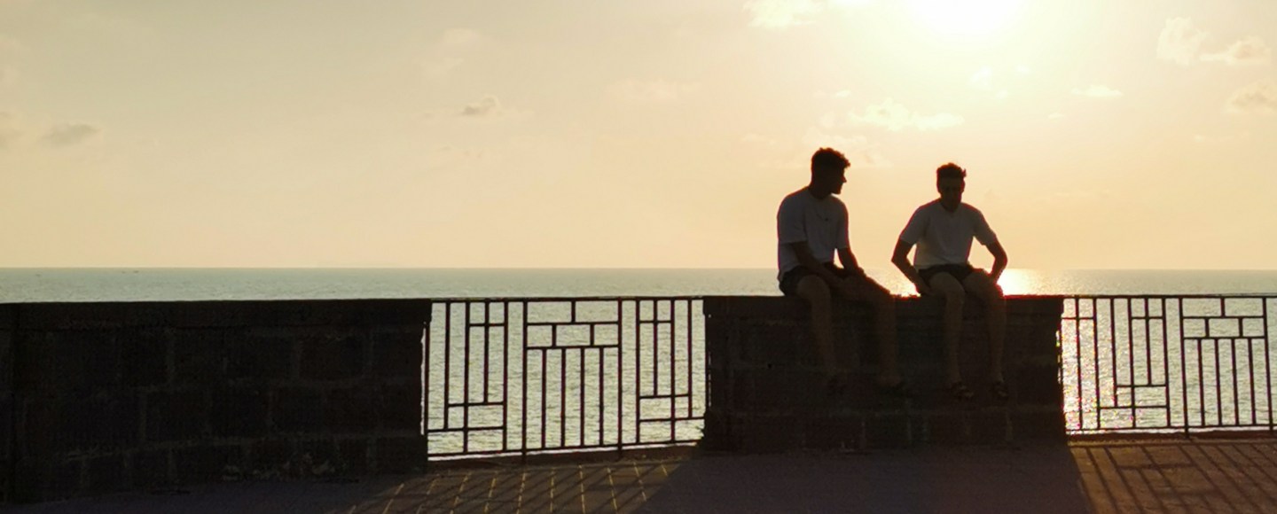 2 boys sitting on a wall as the sun goes down